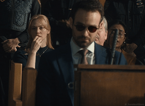 A Woman Covering Her Mouth While A Man In A Suit And Tie Looks On GIF