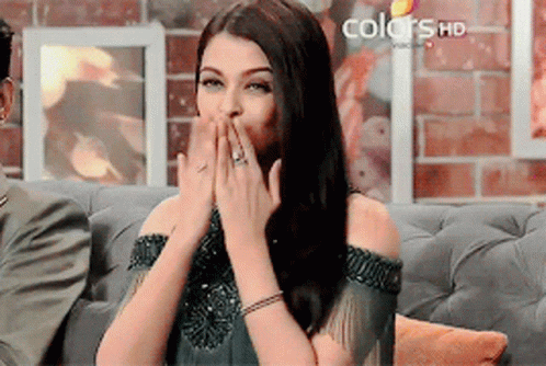 A Woman Covering Her Mouth With Her Hands While Sitting On A Couch With Colors Hd Written On The Bottom GIF