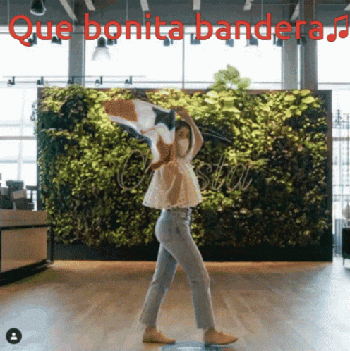 A Woman Dancing In Front Of A Green Wall With Que Bonita Bandera Written Above Her GIF