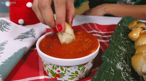 A Woman Dipping A Piece Of Bread Into A Bowl Of Sauce GIF