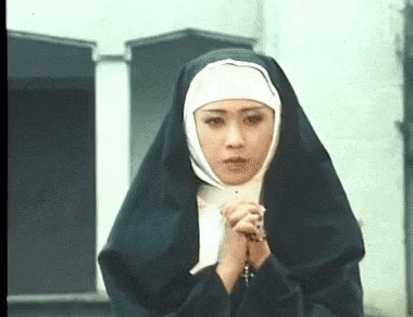 A Woman Dressed As A Nun Is Praying With Her Hands Folded In Front Of A Building . GIF