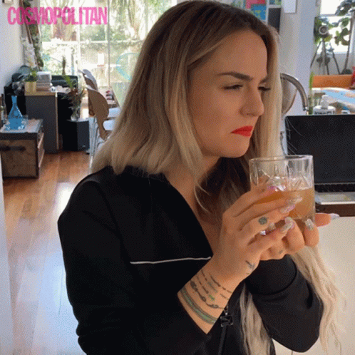 A Woman Drinking From A Glass With Cosmopolitan Written On The Bottom Right GIF