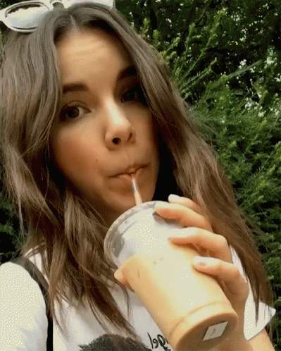 A Woman Drinking Through A Straw From A Cup That Says ' Iced Tea ' On It GIF