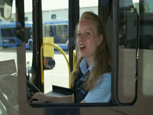 A Woman Driving A Bus With A Blue Shirt That Says ' Unitrans ' On The Front GIF