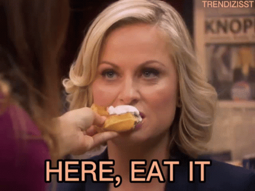 A Woman Eating A Donut With The Words Here Eat It Written Below Her GIF
