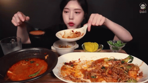 A Woman Eating A Plate Of Food With A Spoon In Her Mouth GIF
