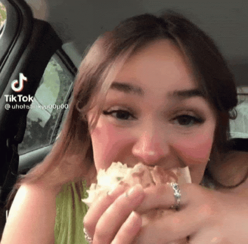 A Woman Eating A Sandwich In A Car With A Tiktok Watermark On The Bottom Right GIF