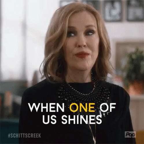A Woman From Schitt 'S Creek Is Smiling And Saying `` When One Of Us Shines '' GIF