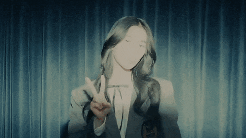 a woman giving a peace sign in front of a curtain