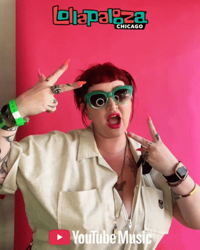 A Woman Giving A Peace Sign In Front Of A Sign That Says ' Lollapaloza Chicago ' GIF