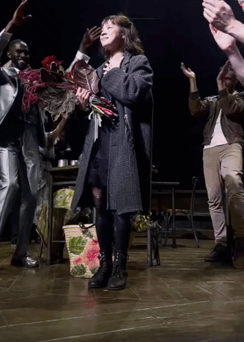 A Woman Holding A Bouquet Of Flowers Stands On A Stage GIF
