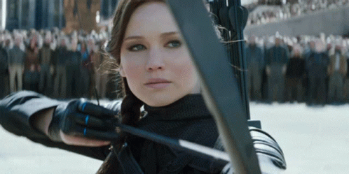 A Woman Holding A Bow And Arrow In Front Of A Crowd Of People GIF