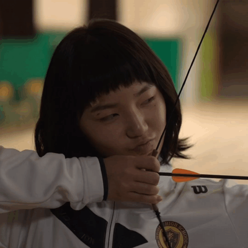 A Woman Holding A Bow And Arrow Wearing A White Wilson Jacket GIF