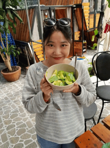 A Woman Holding A Bowl Of Food With A Spoon In Her Hand GIF