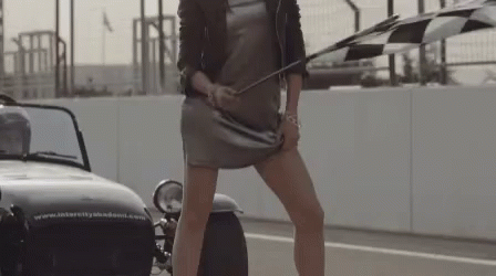 A Woman Holding A Checkered Flag In Front Of A Car That Says Intercity Academy GIF