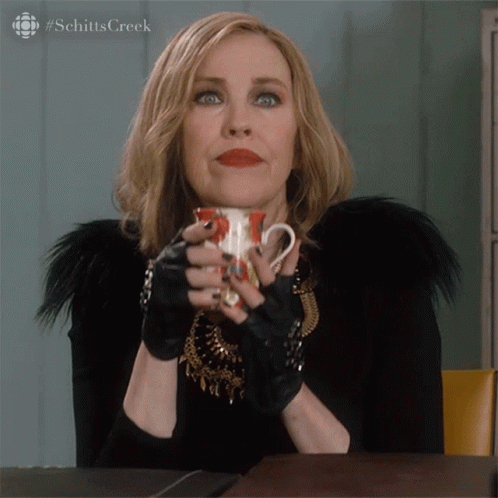 A Woman Holding A Cup Of Coffee With The Hashtag Schitts Creek GIF