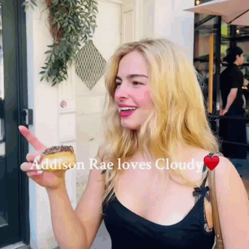 A Woman Holding A Donut With The Words Addison Rae Loves Cloudy GIF