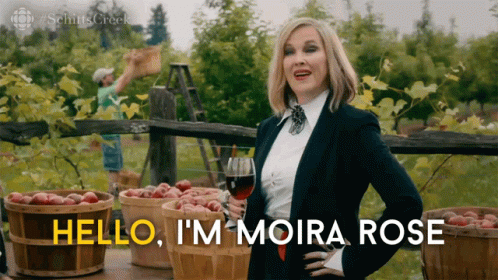 A Woman Holding A Glass Of Wine With The Words Hello I 'M Moira Rose GIF