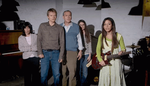a woman holding a guitar stands in front of a group of people