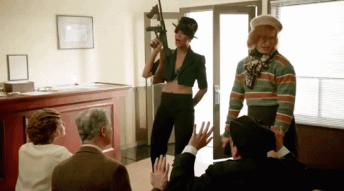 A Woman Holding A Gun Is Surrounded By People GIF
