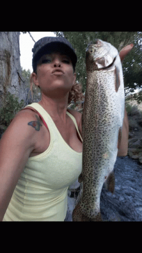 A Woman Holding A Large Fish With A Tattoo On Her Arm GIF