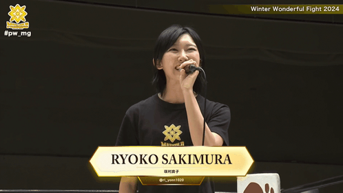 A Woman Holding A Microphone With The Name Ryoko Sakimura On The Screen GIF