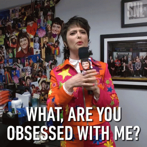 A Woman Holding A Microphone With The Words What Are You Obsessed With Me Below Her GIF