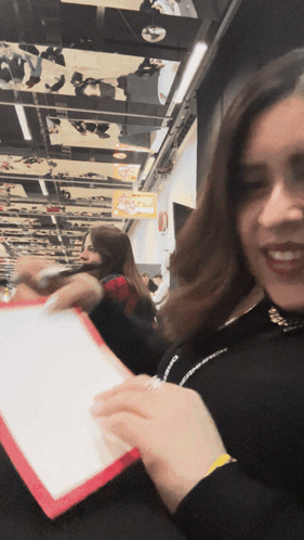 A Woman Holding A Piece Of Paper In Front Of A Sign That Says Pizza GIF