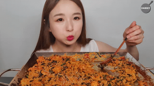 A Woman Holding A Spoon In Front Of A Pan Of Food With The Word Hamzy On The Bottom GIF