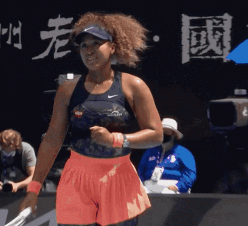 A Woman Holding A Tennis Racquet In Front Of A Sign That Has Chinese Writing On It GIF