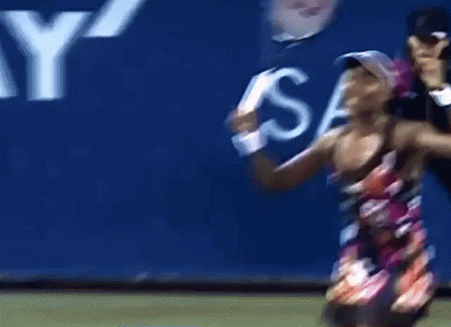 A Woman Holding A Tennis Racquet In Front Of A Sign That Says S. GIF