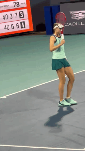 a woman holding a tennis racquet on a court with a cadillac sign in the background