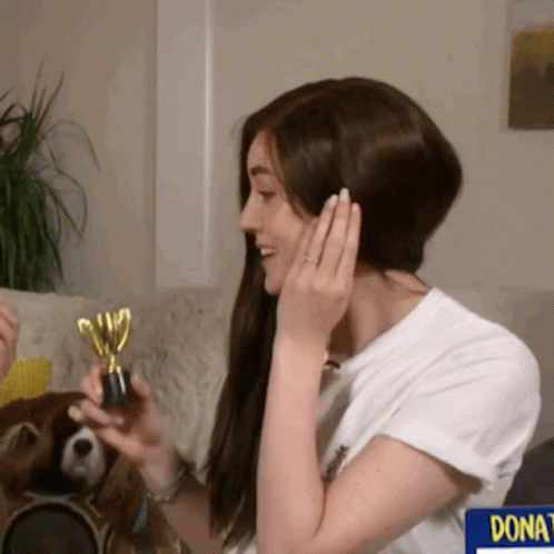 A Woman Holding A Trophy In Front Of A Sign That Says " Donate " GIF