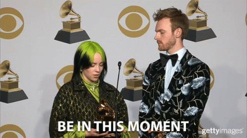 A Woman Holding A Trophy Next To A Man With The Words Be In This Moment On The Bottom GIF