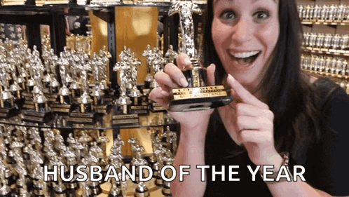 A Woman Holding A Trophy That Says " Husband Of The Year " GIF