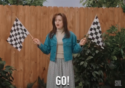 A Woman Holding Two Checkered Flags And Says Go GIF