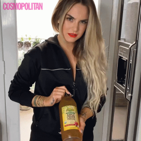 A Woman Holds A Bottle Of Apple Cider Vinegar In Front Of A Cosmopolitan Ad GIF