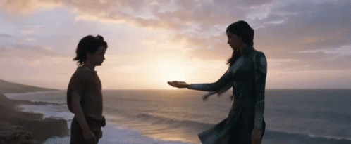 A Woman Holds A Child 'S Hand In Front Of The Ocean At Sunset GIF