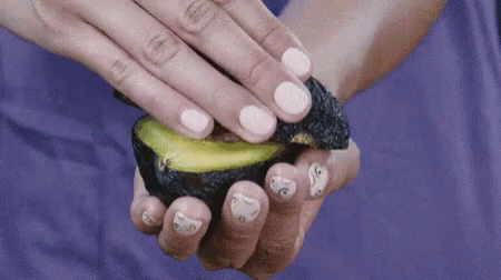 A Woman Holds A Sliced Avocado In Her Hand GIF