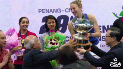 A Woman Holds A Trophy In Front Of A Penang-City Sign GIF