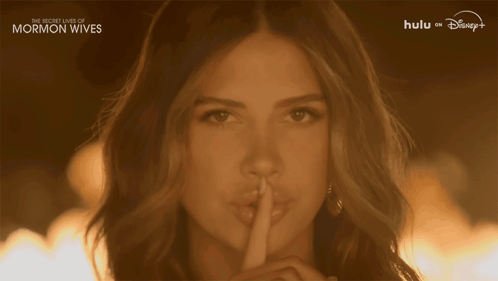A Woman Holds Her Finger To Her Lips With The Words " The Secret Lives Of Mormon Wives " On The Bottom GIF