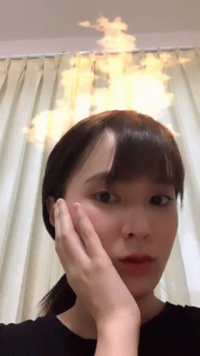 A Woman Holds Her Hand To Her Face With A Fire Coming Out Of Her Head GIF