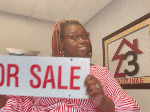A Woman Holds Up A For Sale Sign GIF