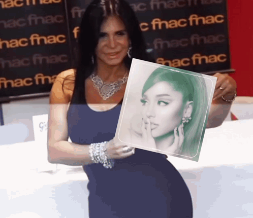 A Woman Holds Up A Picture Of Ariana Grande In Front Of A Fnac Sign GIF