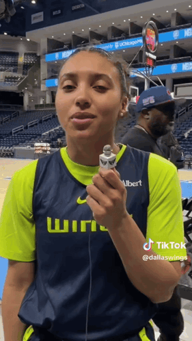 A Woman In A Basketball Uniform Is Holding A Microphone And Talking Into It . GIF