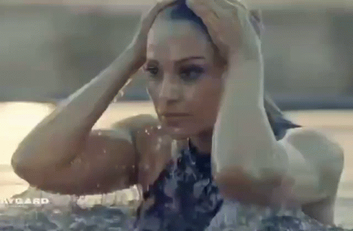 A Woman In A Bathing Suit Is Standing In A Pool Holding Her Head . GIF