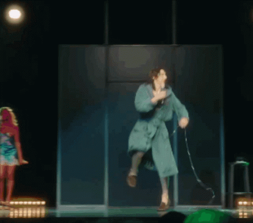 A Woman In A Bathrobe Is Dancing On A Stage GIF