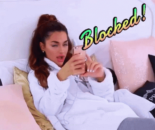 A Woman In A Bathrobe Is Laying On A Bed Looking At Her Cell Phone With The Word Blocked Behind Her GIF