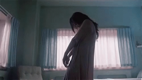 A Woman In A Bathrobe Is Standing In A Bedroom . GIF