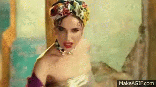 A Woman In A Bathtub Wearing A Turban And A Necklace Is Making A Funny Face . GIF